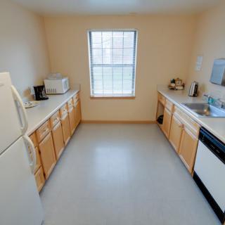 A tidy and compact kitchen with wooden cabinets, featuring appliances like a refrigerator, microwave, and dishwasher.