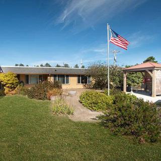 A suburban house with a neatly landscaped yard and a flagpole displaying the American flag under a clear blue sky.