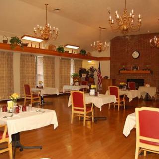 An elegant dining room with chandeliers, red chairs, and a brick wall fireplace.