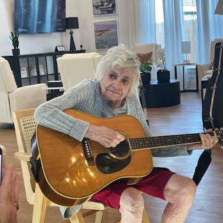 An elderly woman enjoying playing the guitar in a cozy living room.