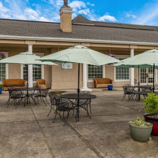 A well-furnished outdoor patio with tables, chairs, and umbrellas in front of a building.