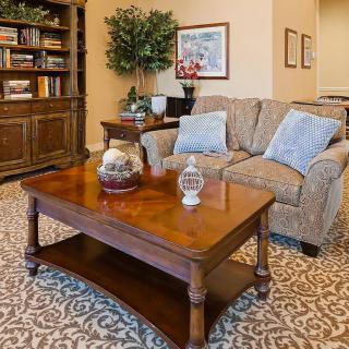 A cozy living room with a patterned carpet, a comfortable sofa, and a wooden coffee table adorned with decorative items. A bookshelf and an indoor plant add to the inviting ambiance.