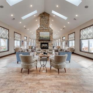 A spacious and modern living room featuring a central fireplace, multiple seating areas, wooden flooring, and natural light from skylights.