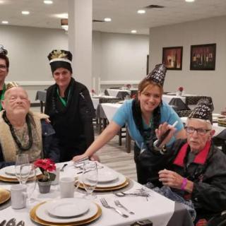 A group of people wearing festive hats gather around a table set for a celebration.
