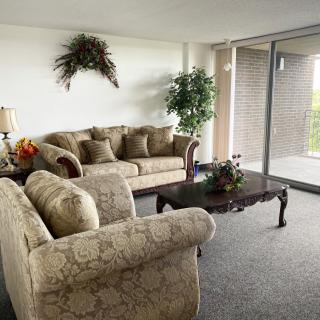 A cozy living room with elegant sofas and a coffee table, adorned with indoor plants and natural light streaming through large glass doors.