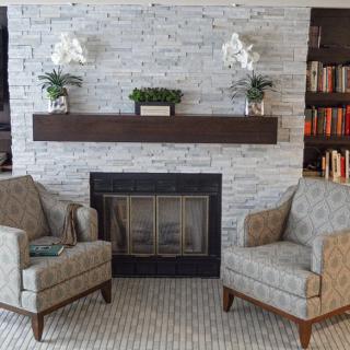 A cozy living room area with a fireplace, two armchairs, and decorative elements including books and indoor plants.