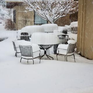 A winter scene with a table and chairs covered in a thick layer of snow.