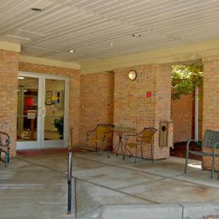 A covered building entrance with chairs and tables set against brick walls.