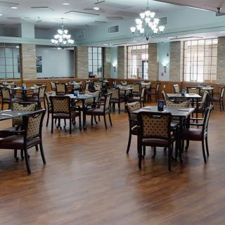 An empty dining area with neatly arranged tables and chairs under elegant chandeliers.