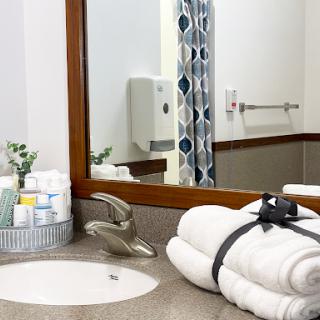 A neatly organized bathroom featuring plush white towels, essential toiletries, and a stylish mirror.