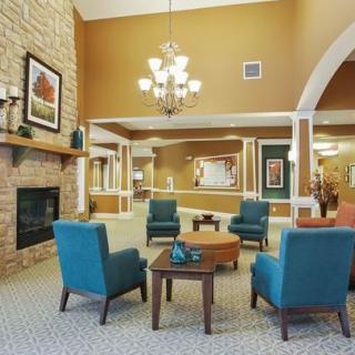 A cozy living room with a warm color palette, featuring comfortable armchairs around a coffee table and a fireplace under a decorative chandelier.