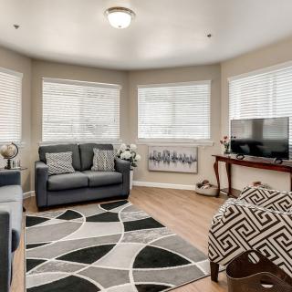 A cozy living room with a sofa, armchair, and a patterned rug on hardwood flooring.