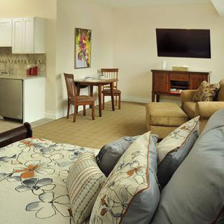 A cozy living space featuring a comfortable sofa, a wall-mounted television, a small dining area, and a kitchenette.