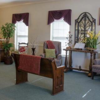 A well-decorated living room with a wooden desk, chairs, and plants by the windows.
