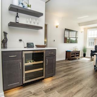 A modern kitchen space featuring a wine fridge and wooden shelves, leading into an open living area.