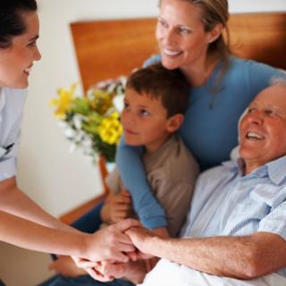 A caregiver interacts warmly with a family, bringing joy to an elderly man and his loved ones.