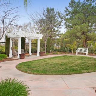 A well-maintained garden featuring a gazebo, bench, and lush lawn surrounded by trees.