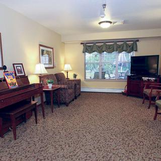 A cozy living room with a piano, sofa, TV, and carpeted flooring.