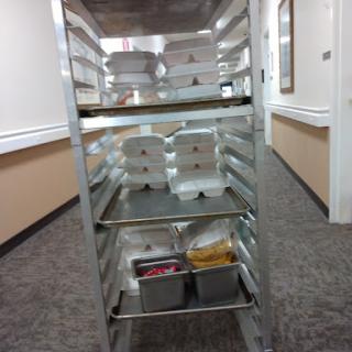 A food cart filled with containers ready for service in a dining area.