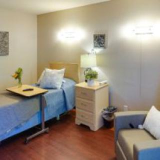 A well-furnished bedroom featuring a single bed, nightstand with a lamp, and an armchair.
