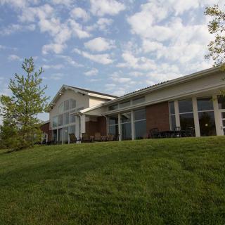 A view of a large building with a sloped grassy hill and a partly cloudy sky.