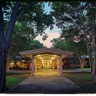 An illuminated building entrance with a pathway surrounded by trees at dusk.