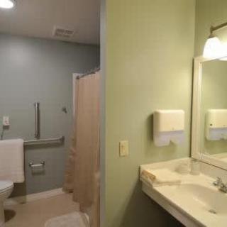 A clean, accessible bathroom with a sink, mirror, toilet, and handrails.
