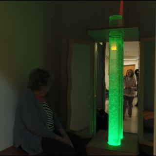 A person sits next to a glowing green bubble tube in a sensory room.