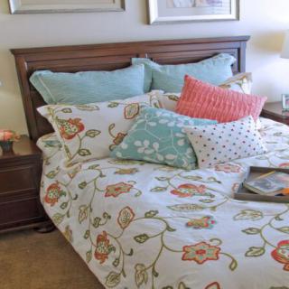 A cozy bedroom with a floral-patterned bedspread and an arrangement of colorful pillows.