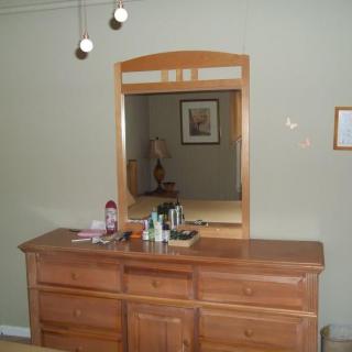 A wooden dresser with an attached mirror, topped with various items, set in a bedroom.