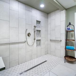 A modern walk-in shower with tiled walls and floor, equipped with grab bars and a handheld showerhead.