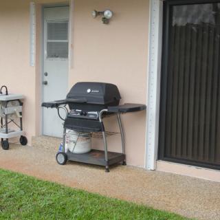 An outdoor patio area with a barbecue grill and propane tank next to a door and window.