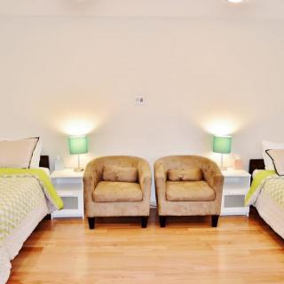 A cozy bedroom featuring twin beds, two armchairs, and stylish lamps on nightstands.