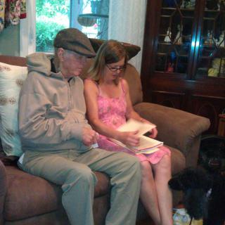 Two people sitting on a couch reading together, with a dog nearby.