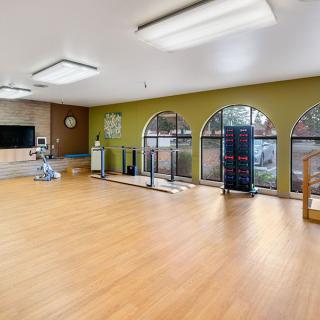A spacious exercise room with hardwood floors, large mirrors, and ample natural light.
