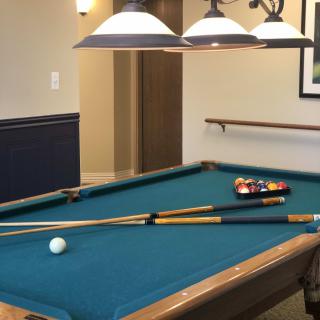 A well-lit game room featuring a billiard table with pool cues and balls ready for play.