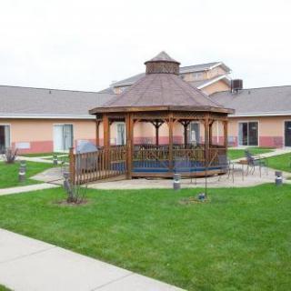 A charming wooden gazebo situated in the middle of a grassy courtyard surrounded by buildings.