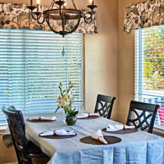 A cozy dining room with a neatly set table, surrounded by natural light from large windows.