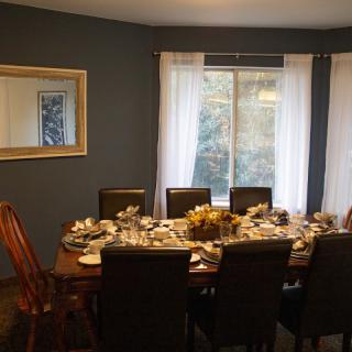 A dining room with a table set for a meal, featuring elegant chairs and a large window with curtains.