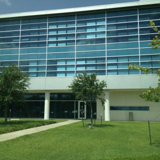 A modern building with a glass facade surrounded by a well-maintained lawn and trees.