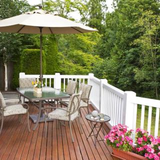 A wooden deck with patio furniture and an umbrella, surrounded by lush greenery.