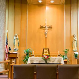 A church altar with religious symbols and a cross, surrounded by statues and plants.
