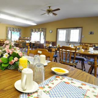 A cozy dining room set up for a meal, featuring wooden tables and chairs with floral decorations.