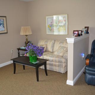 A cozy living room area with a sofa, table, lamp, and framed artwork on the walls.