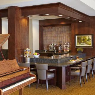 A cozy bar area with a wooden piano and seating arrangement, featuring elegant decor and artwork.