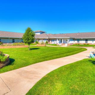 A scenic view of a well-maintained lawn and garden with a winding pathway leading to a building under a clear blue sky.