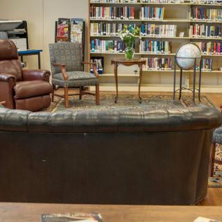 A cozy library setting featuring a sofa, chairs, and a globe in front of a well-stocked bookshelf.