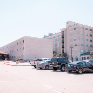 A parking lot in front of a large multi-story building on a clear day.