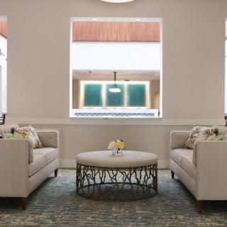 A modern living room with neutral-colored sofas facing each other, a round coffee table in the center, and large windows providing natural light.