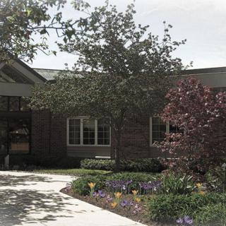 A view of a building surrounded by trees and flowers with a pathway leading to the entrance.
